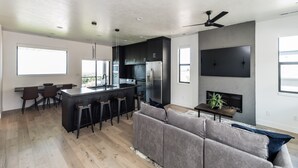Une cuisine moderne avec un coin bar, un canapé gris et un téléviseur à écran plat fixé au mur.