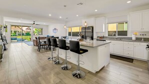 Een moderne keuken met witte kasten, een groot eiland en barstoelen.