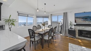 A spacious dining area with a large table and chairs, a kitchen area with a modern stove, and a large window offering a view of the sea. - Top Floor Unit with Panoramic Views Steps to the beach with 3 Parking Spots!  (Manhattan Beach)