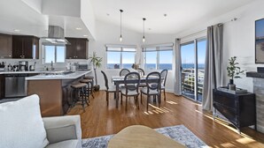 A modern kitchen with a central island, dining area with chairs, and large windows offering a view of the sea. - Top Floor Unit with Panoramic Views Steps to the beach with 3 Parking Spots!  (Manhattan Beach)