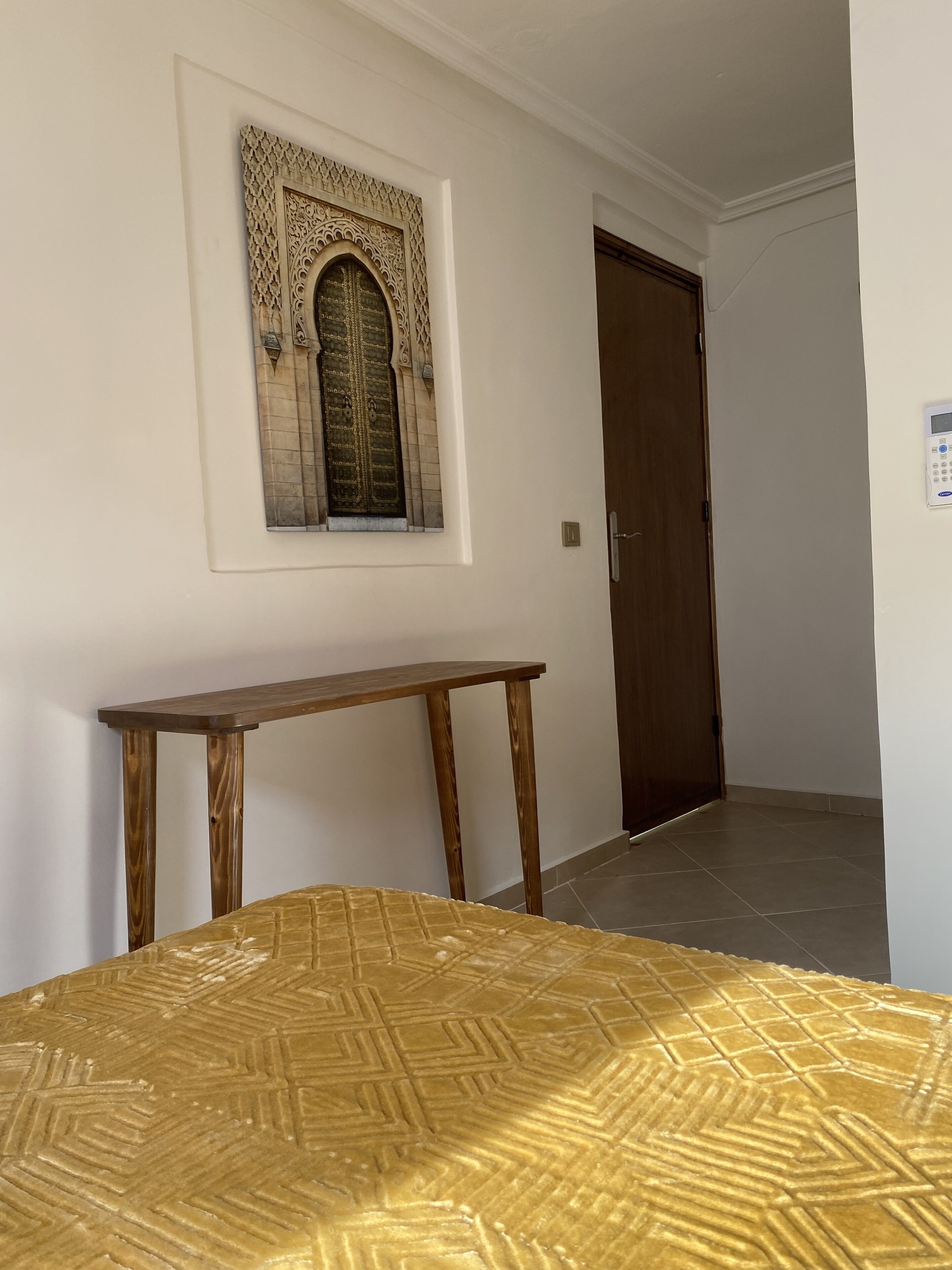 A room with a bed, a wooden console table, a decorative wall piece, and a door.