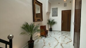A hallway with a skylight, marble flooring, potted plants, a wooden cabinet, and a door with decorative panels. - Riad Jbara 2 (Rabat)