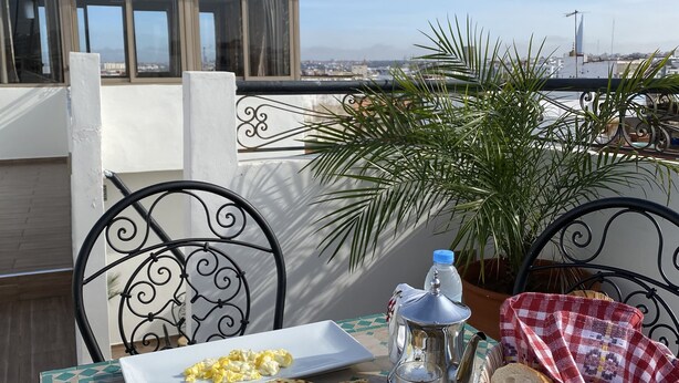 A table set with breakfast items including eggs, bread, and juice, on a terrace with a view of the city. - Riad Jbara 2 (Rabat)