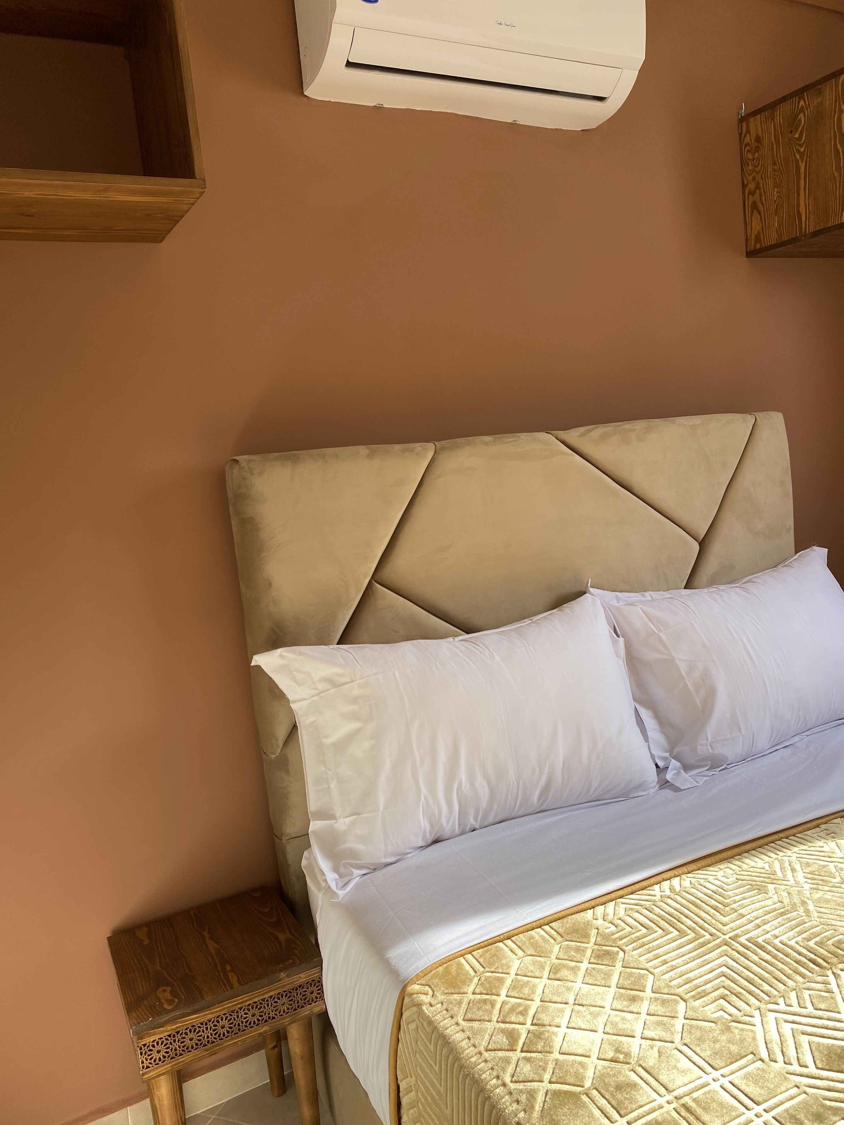 A bed with a beige headboard, white pillows, and a patterned bedspread.