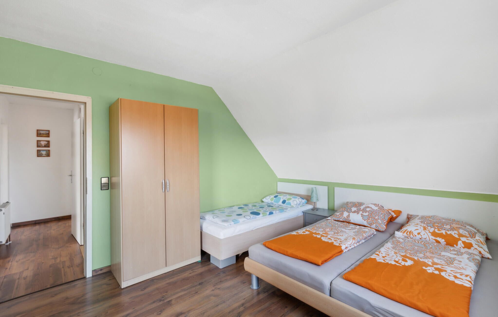 A bedroom with two single beds, a wardrobe, and a door leading to another room.