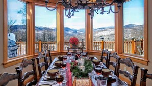A dining area with a table set for six, large windows offering a mountain view, and a chandelier above.