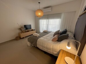 A modern bedroom with a bed, bedside table, TV, and a hanging light fixture.