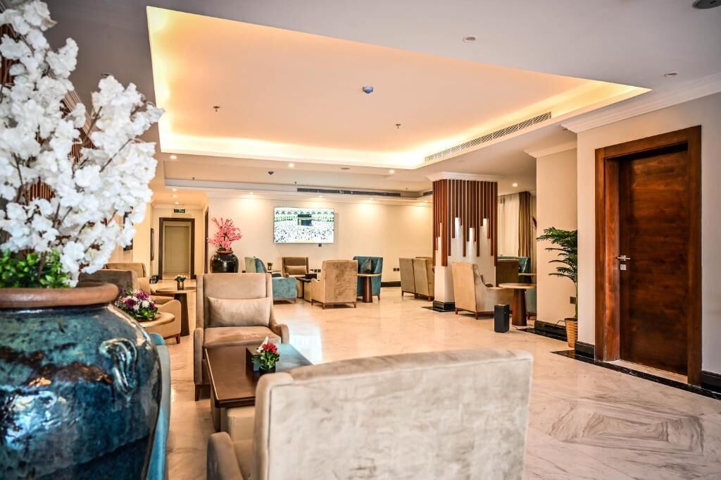 A modern lobby with comfortable seating, a large digital screen, and a decorative vase.