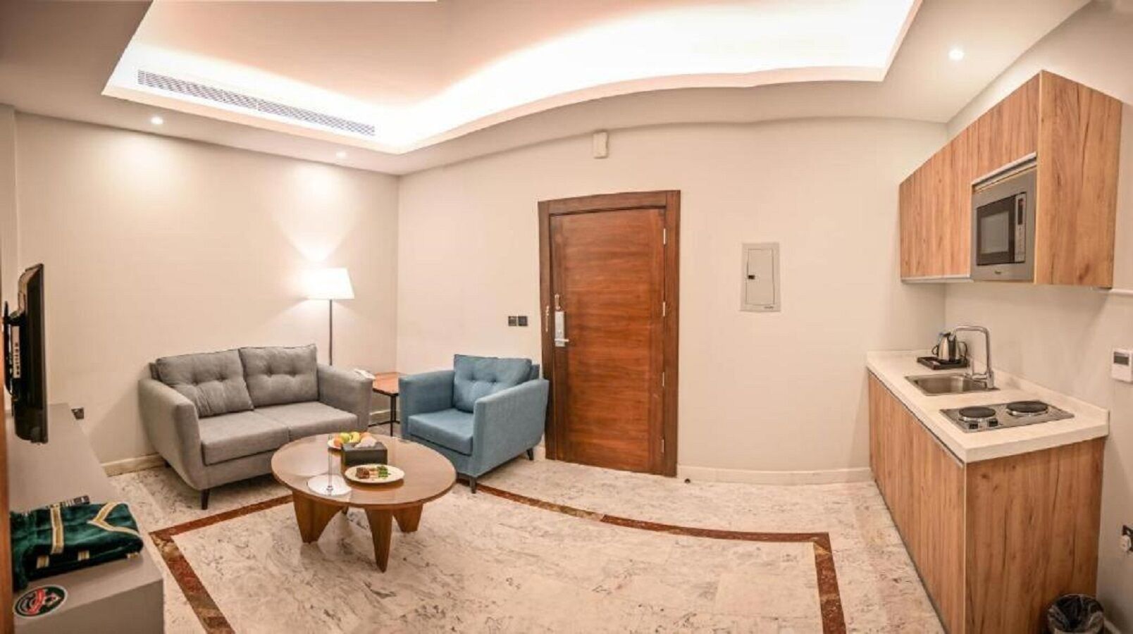 A compact living space with a sofa, armchair, coffee table, and a kitchenette with a microwave and stove.