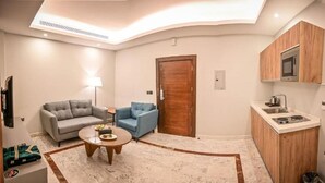 A compact living space with a sofa, armchair, coffee table, and a kitchenette with a microwave and stove.