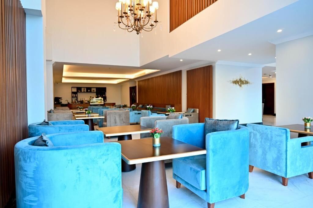Una hall moderna di un hotel con sedute imbottite blu, un lampadario e un'area bar sullo sfondo.