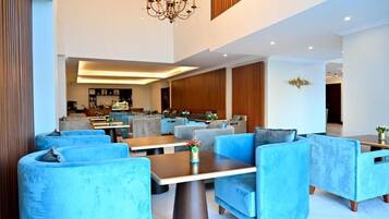 Una hall moderna di un hotel con sedute imbottite blu, un lampadario e un'area bar sullo sfondo.