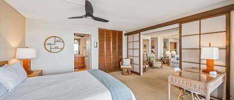 Ein Hotelzimmer mit einem Bett, einem Schreibtisch, einem Stuhl, einem Deckenventilator und einer Schiebetür zu einem Badezimmer.
