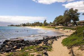 A beach with rocky shoreline, clear water, and a path leading to the beach.