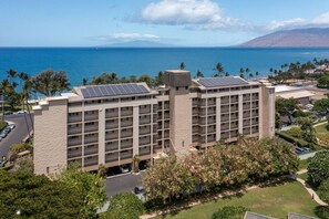 A multi-story hotel with a central tower, solar panels on the roof, and a view of the ocean.