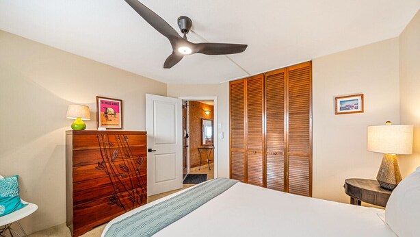 Une chambre d’hôtel comprenant un lit, un bureau, une armoire, un ventilateur de plafond et une porte donnant sur une autre pièce.