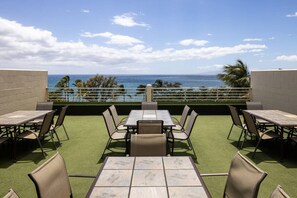 An outdoor patio with tables and chairs, a view of the ocean, and a clear sky.