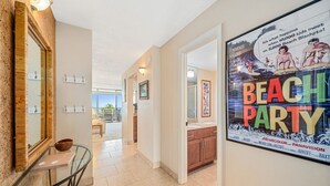 Un couloir orné d’une affiche faisant la promotion d’une fête sur la plage, avec un miroir et un coin repas comprenant une table et des chaises.