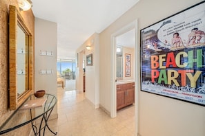 A hallway with a poster advertising a beach party, a mirror, and a dining area with a table and chairs.
