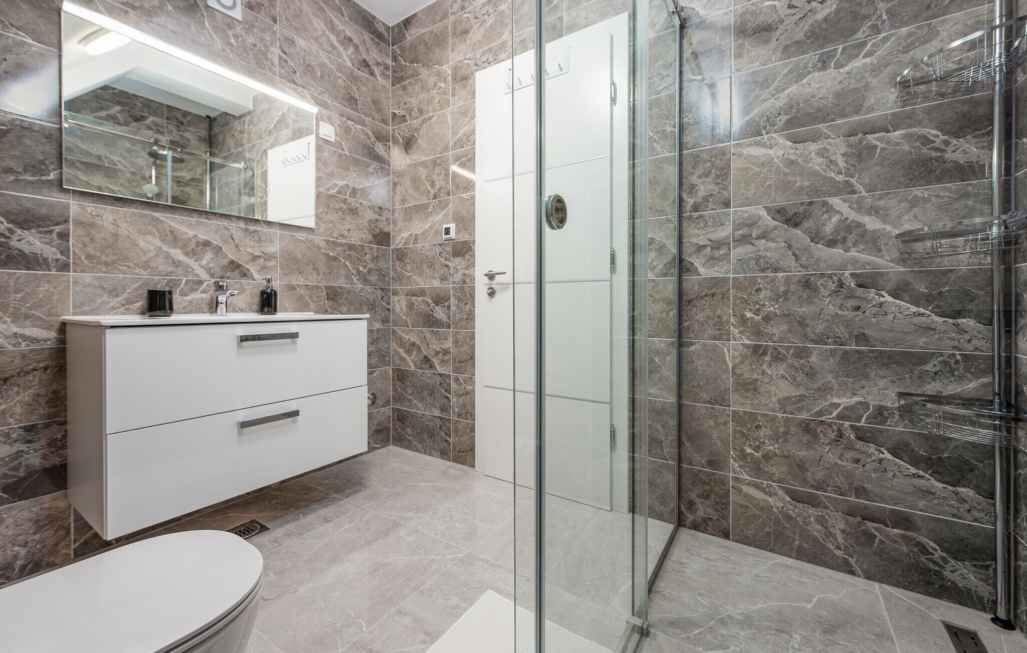 Un baño moderno con cabina de ducha de vidrio, tocador blanco con cajones y un espejo grande.