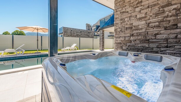 A hot tub with a stone wall backdrop, a pool, and outdoor seating. - Lovely home in Debelo Brdo with sauna (Debelo Brdo)