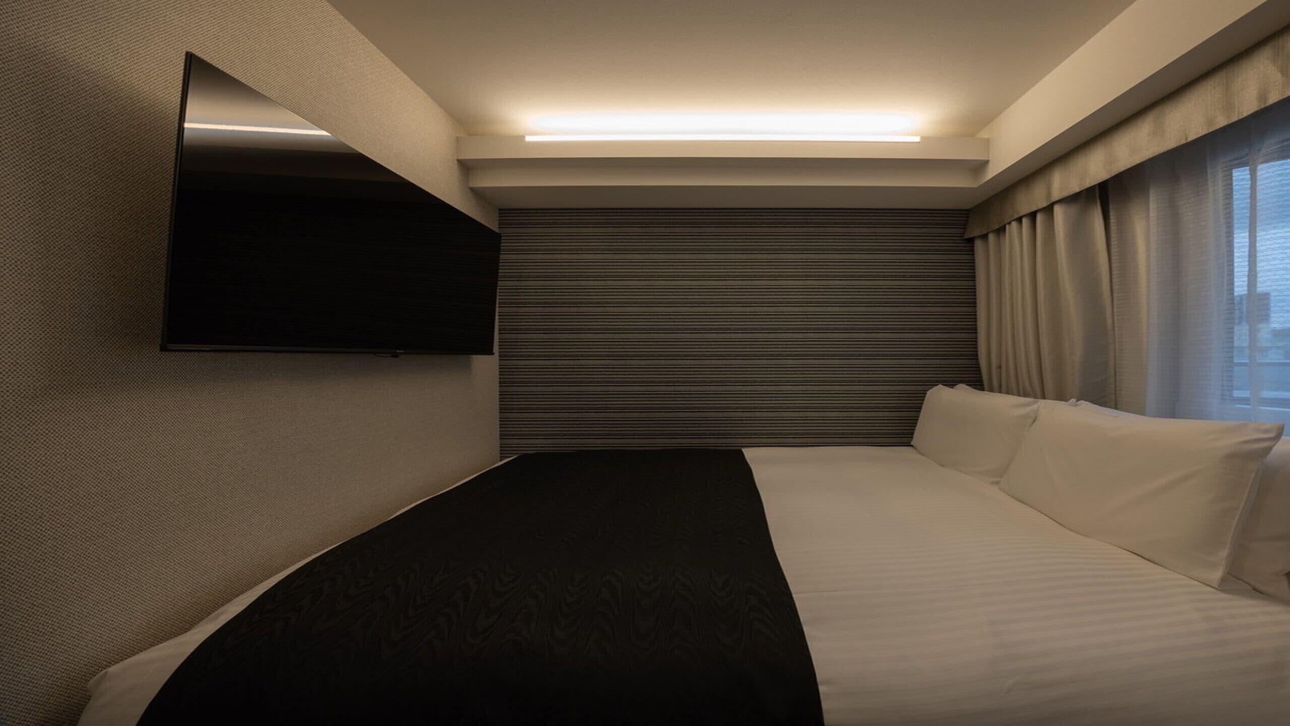 Une chambre d’hôtel moderne équipée d’un lit, d’un téléviseur à écran plat fixé au mur et d’une fenêtre avec des rideaux.