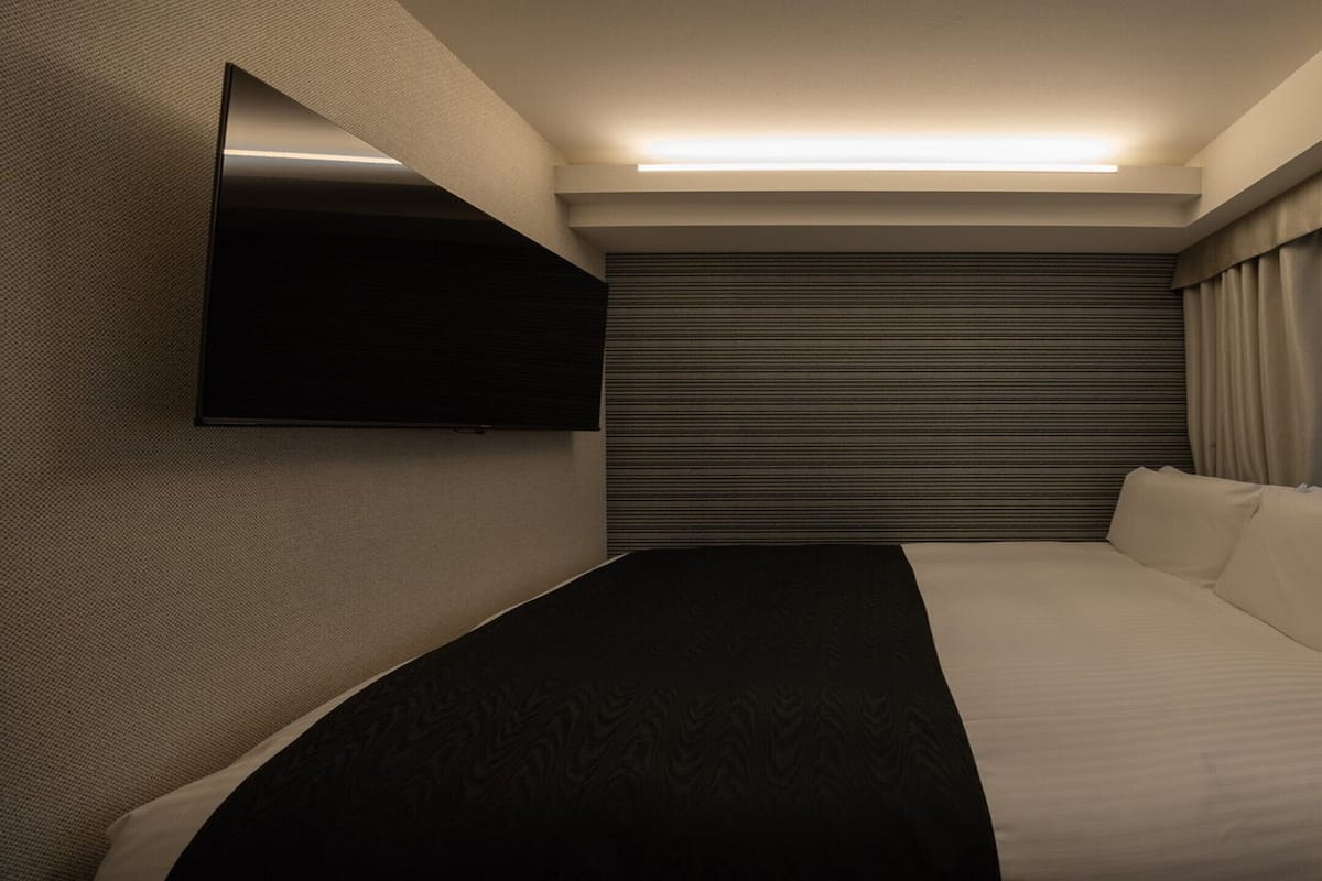 Une chambre d’hôtel moderne équipée d’un lit, d’un téléviseur à écran plat fixé au mur et d’une fenêtre avec des rideaux.