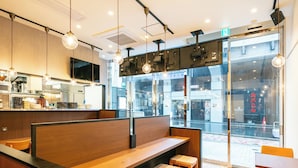 A modern restaurant with wooden booths, a kitchen area, and a view of the street through large windows. - APA Hotel Ueno Okachimachi Ekimae Minami (Tokyo)
