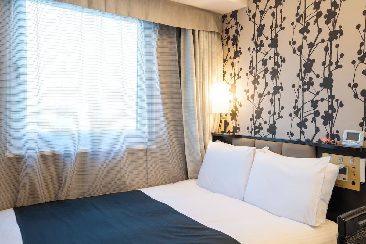 Une chambre d’hôtel avec un lit, une table de chevet avec une lampe et un mur orné d’un motif floral.