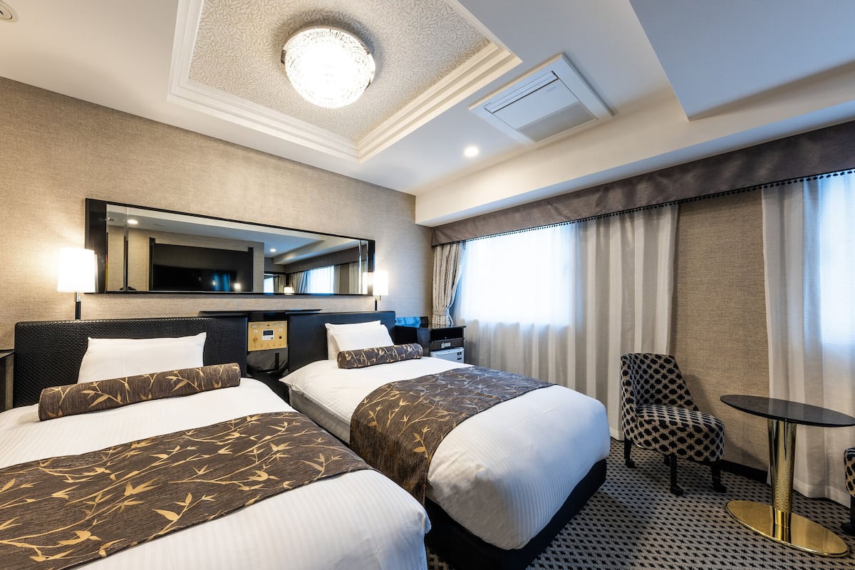 Une chambre d’hôtel avec deux lits, un bureau, une chaise, une table ronde et un grand miroir.