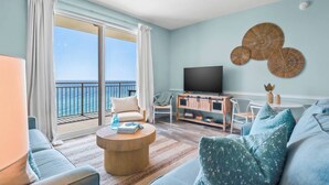 Een ruime woonkamer met een groot raam met uitzicht op de zee, een flatscreen televisie en een houten tv-meubel.