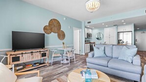 Een moderne woonkamer met een flatscreen televisie, een bank, een salontafel en een eethoek met een witte tafel en stoelen.