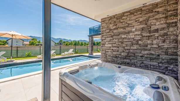 Un área de piscina moderna al aire libre con un jacuzzi, cielos despejados y vistas a la montaña.