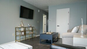 A living room with a sofa, a coffee table, a TV mounted on the wall, and a bookshelf. - Oasis on Empire near Buckeye Lake! (Thornville)