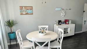 A dining area with a round table, white chairs, a potted plant, a welcome sign, and a coffee station. - Oasis on Empire near Buckeye Lake! (Thornville)