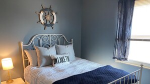 A neatly made bed with a white headboard and a decorative ship's wheel above it. - Oasis on Empire near Buckeye Lake! (Thornville)