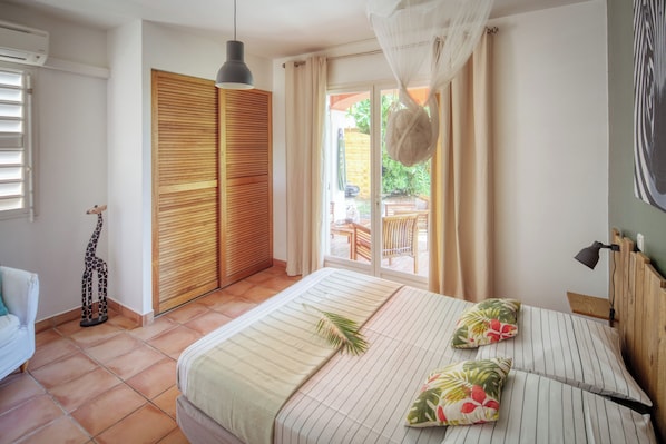 A bedroom with a bed, a wooden wardrobe, a small giraffe decoration, and a view of the outside.