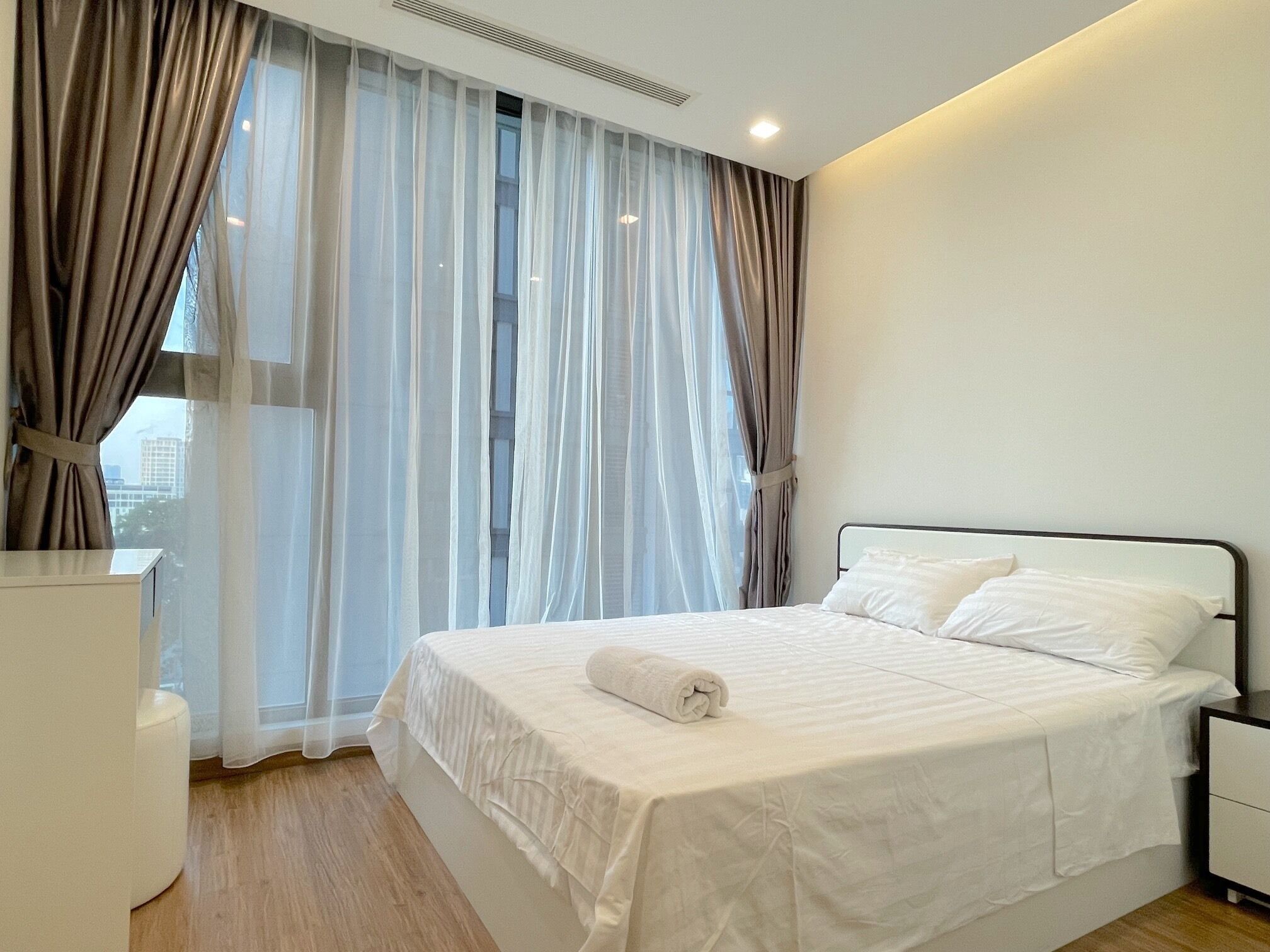 Una habitación de hotel moderna con una cama grande, ropa de cama blanca, una mesita de noche y cortinas traslúcidas.