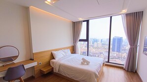 Moderni hotellihuone, jossa on puinen sänky, työpöytä tuolilla ja suuri ikkuna, josta avautuu näkymä kaupunkiin.