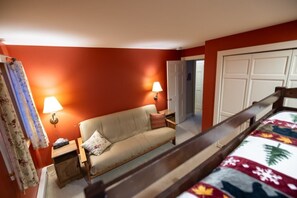A hotel room with a bed, a sofa, two bedside lamps, a nightstand, and a door leading to another room.