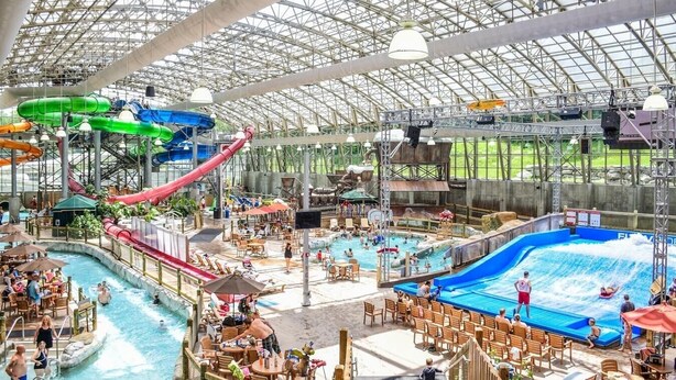 Parque acuático interior con varias piscinas, toboganes y una zona cubierta con asientos.