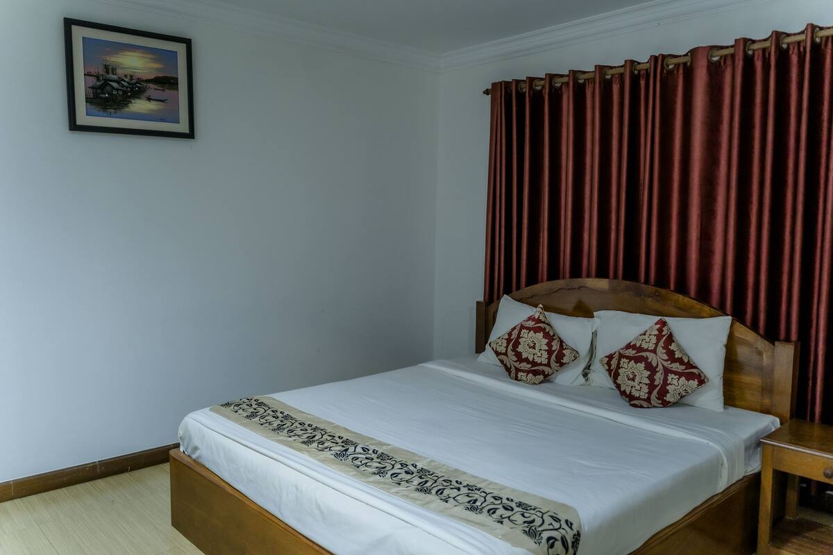 A neatly made bed with a wooden headboard, a bedside table, and a framed picture on the wall.