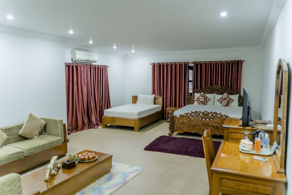 A well-lit hotel room with a bed, a sofa, a wooden desk, and a television.
