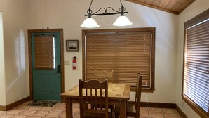 A dining area with a wooden table and chairs, a blue door, a window with blinds, and a ceiling light fixture. - Find your Paradise 1, right in the middle of what brings you to Ruidoso! (Ruidoso)
