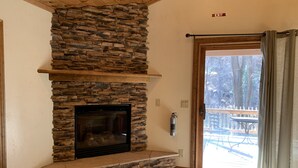 A stone fireplace with a wooden mantel, a fire extinguisher, and a view of a wooden deck outside. - Find your Paradise 1, right in the middle of what brings you to Ruidoso! (Ruidoso)