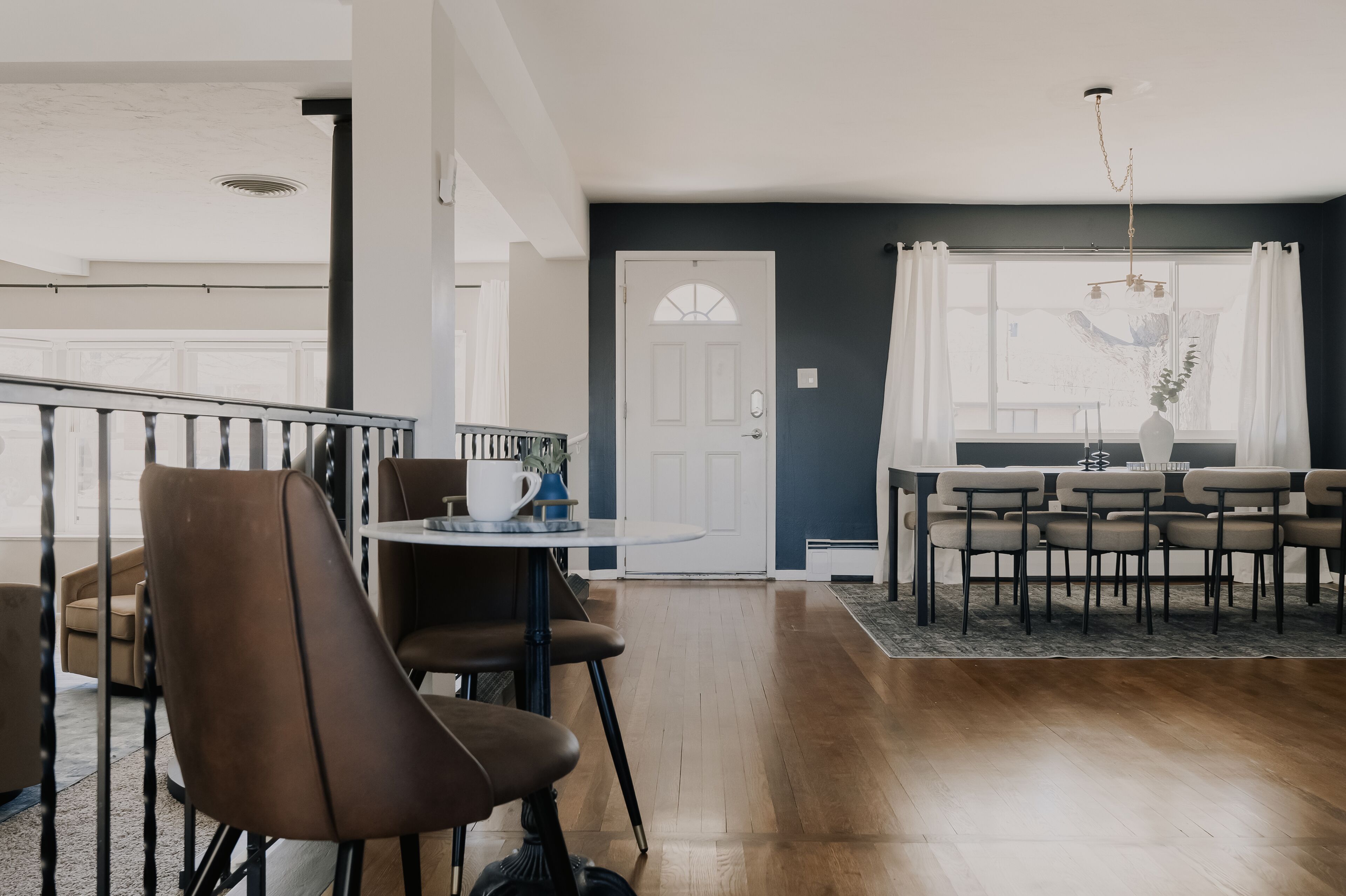 A dining area with a round table and chairs, a staircase, and a view of the outdoors.