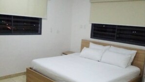 Een slaapkamer met een houten bed, witte beddengoed, een raam met zonwering en een airconditioner aan de muur.