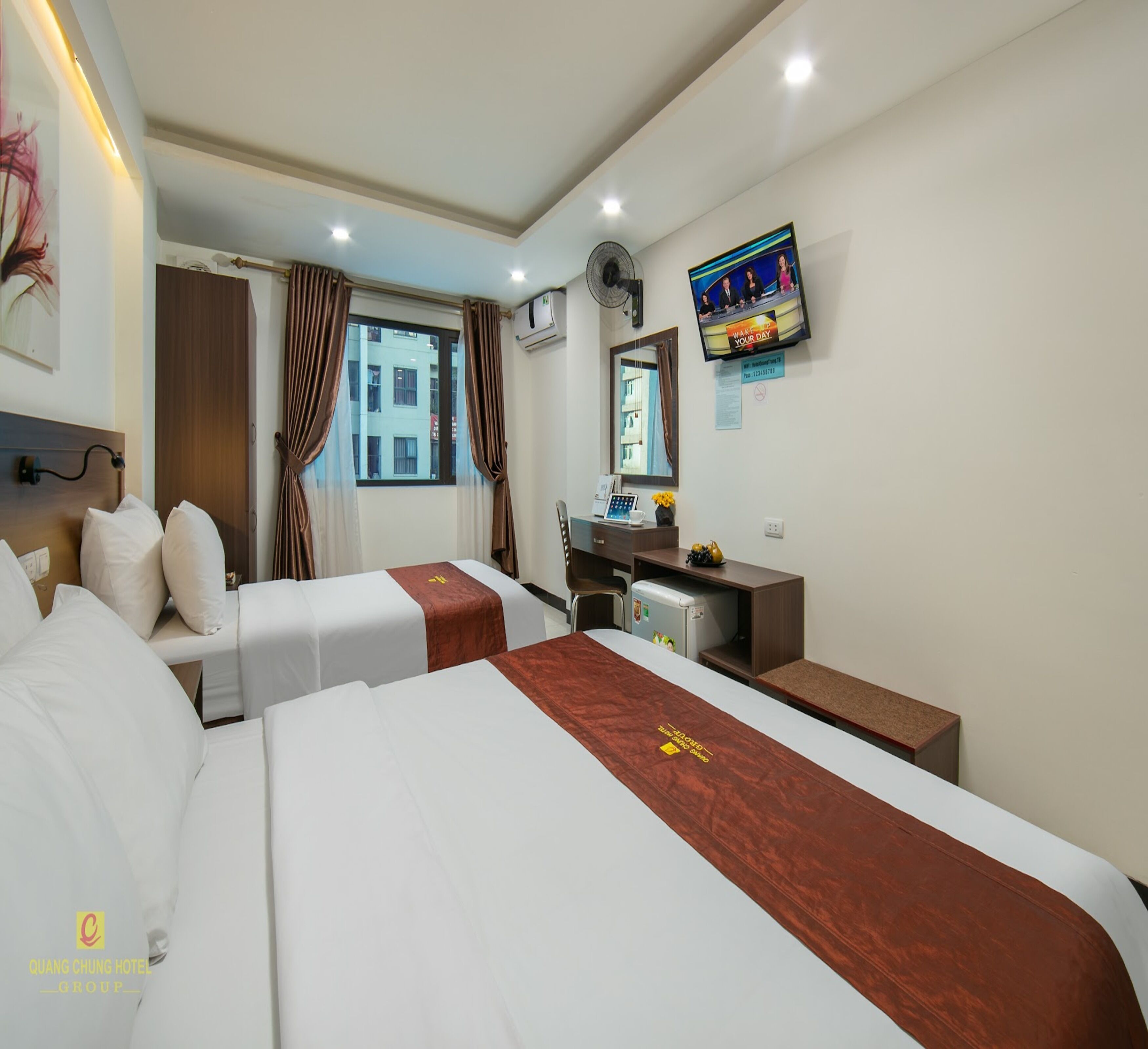 Una habitación de hotel con dos camas, un escritorio, una silla, un televisor y una ventana con cortinas.