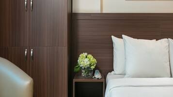 A hotel room with a bed, a nightstand with a vase of flowers, and a wooden wardrobe.