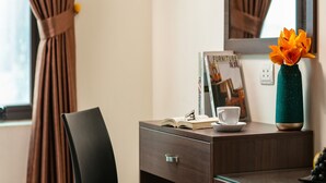 A hotel room with a desk, a chair, a vase with flowers, a cup, and a book. - Quang Chung Hotel (Hanoi)